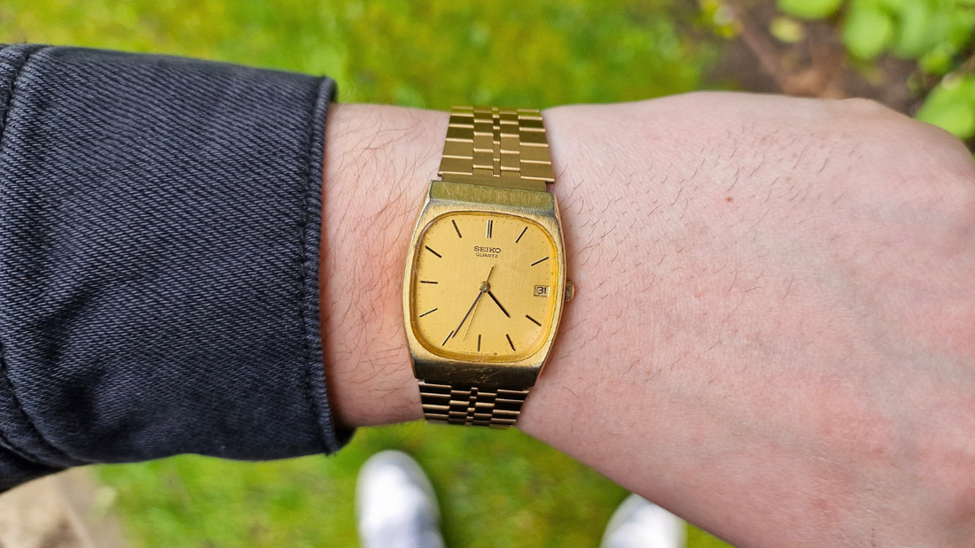 Gold Seiko Tank on the wrist, green grass background, vintage watch, wrist shot