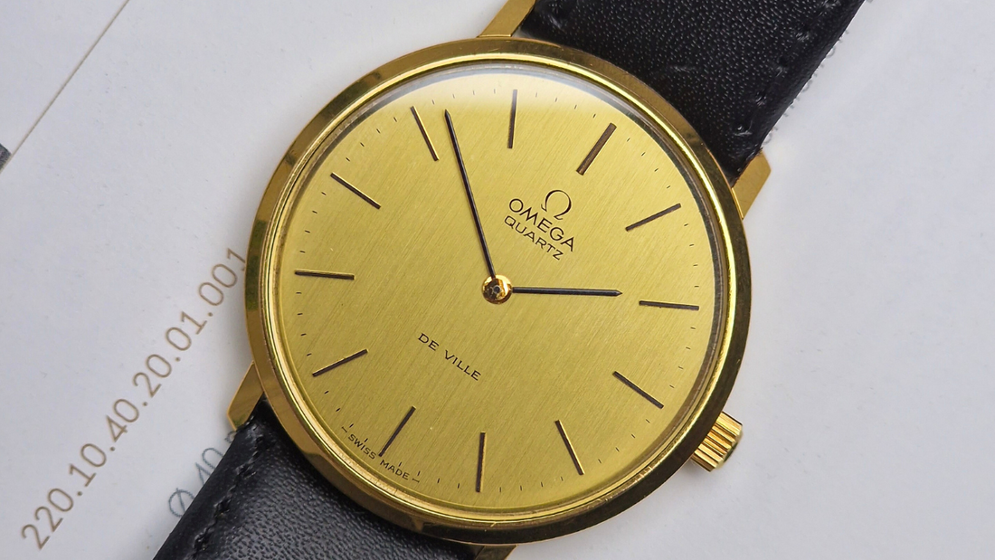 Vintage Omega De Ville Quartz watch with gold dial, black hour markers, and black leather strap on white background