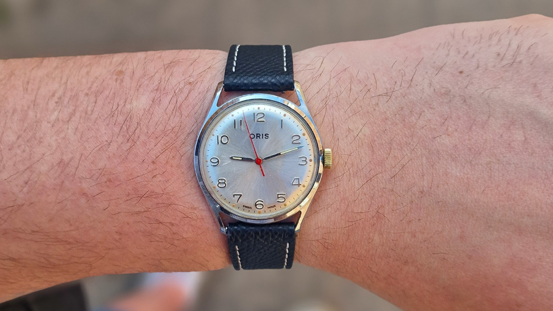 Vintage 1960s Oris manual wind watch with gold sunburst dial, 34mm stainless steel case, and black leather Cartier-style strap shown on display