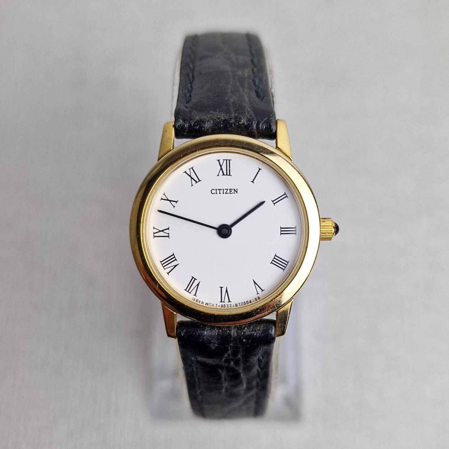 Front view of a vintage Citizen ladies watch with a gold-plated case, Roman numeral white dial, black leather strap, and cabochon crown.